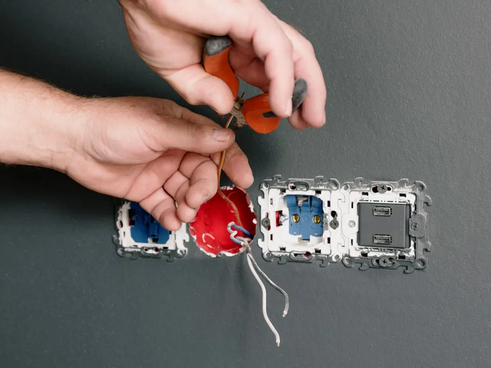 Electrician repairing exposed wiring at wall sockets