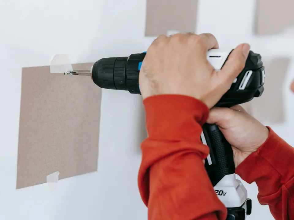 Hands fixing a screw into an interior wall using a cordless drill and a paper positioning template